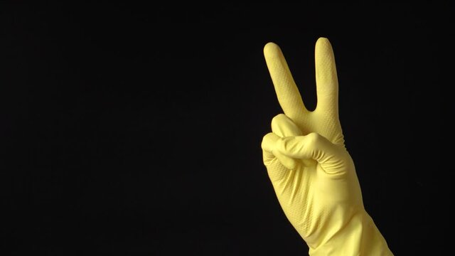 Hand in yellow rubber cleaning glove showing victory sign on black background