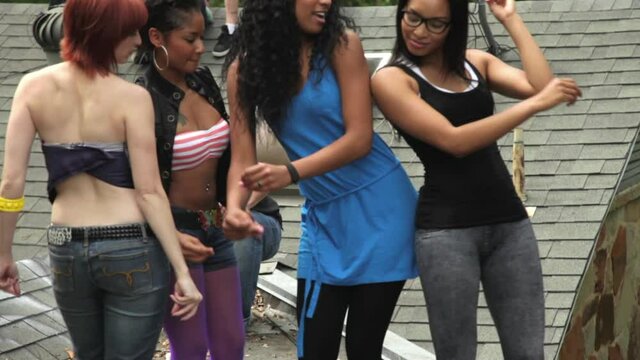 Group of friends hanging out on rooftop having party, girls dancing, mans taking camera phone pics