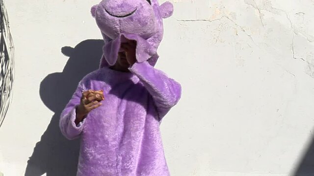 Black man in a hippo outfit eats a slice of pizza