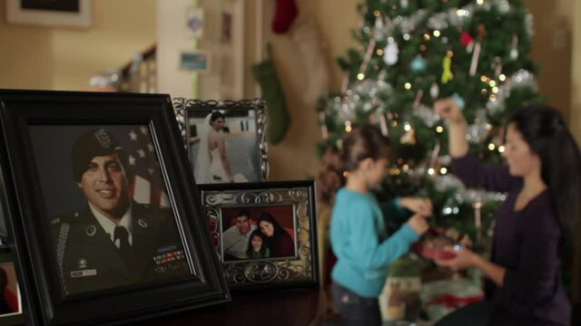 Mother and daughter decorating Christmas tree with framed portrait of father in military uniform