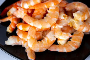 Peeled shrimp on black plate on white background