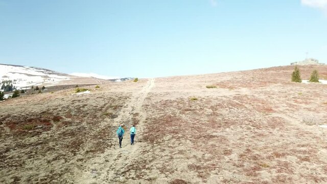 A drone capture of a couple with big backpacks hiking to Seiner Kreuz, a peak in Austrian Alps. Cross on the peak. There are a few snow fields around. Early spring in the mountains. Wanderlust
