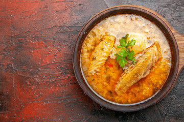 top close view chicken soup in wooden bowl with handle on dark red background with free space