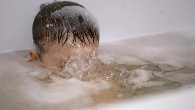 Boy Bathes in Water with Foam in Bathtub, Submerges Under Water, Blows Bubbles