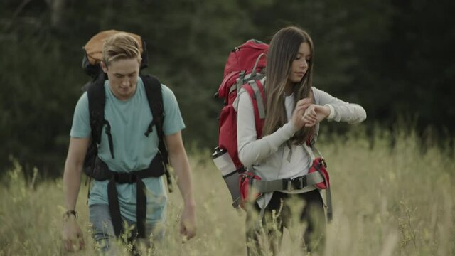 Teenage couple hiking in field then girl talking to smart watch / Tibble Fork, Utah, United States