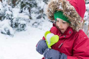 Side view portrait of child girl making snowballs while walking near the house. Winter activities for kids outside