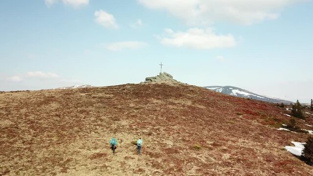 A drone capture of a couple with big backpacks hiking to Seiner Kreuz, a peak in Austrian Alps. Cross on the peak. There are a few snow fields around. Early spring in the mountains. Wanderlust
