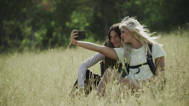 Teenage girls sitting on hill posing for cell phone selfies / Tibble Fork, Utah, United States