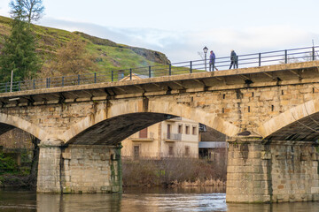Fototapeta premium Stone bridge Puebla de Sanabria with people walking in a sunset, catalogued as one of the most beautiful villages in Spain