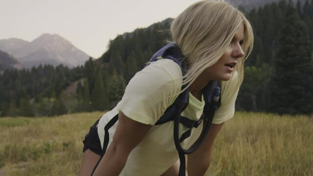 Teenage girl with backpack in field resting then checking wristwatch and running / Tibble Fork, Utah, United States