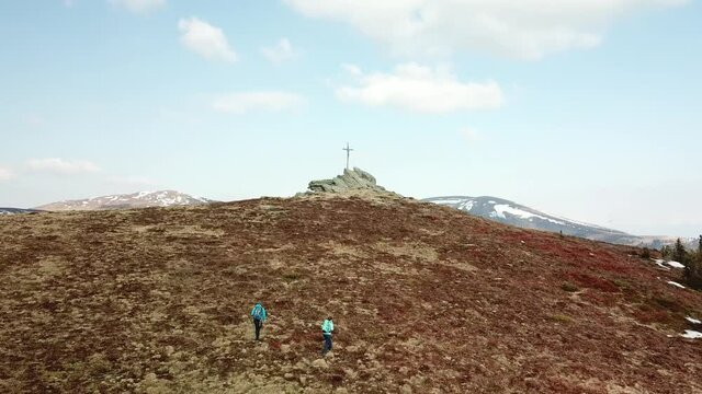 A drone capture of a couple with big backpacks hiking to Seiner Kreuz, a peak in Austrian Alps. Cross on the peak. There are a few snow fields around. Early spring in the mountains. Wanderlust
