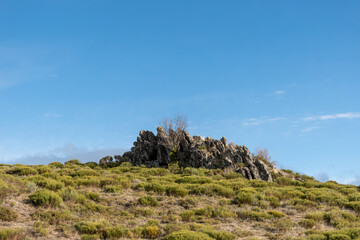 Horizontal landscape view of some rocks at the top of a mountain with a green meadow on a sunny day