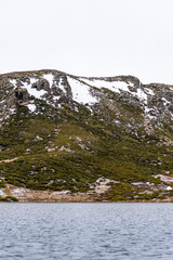 Vertical panoramic landscape image from a boat in the middle of the water with snowy mountains in the background on a cloudy day