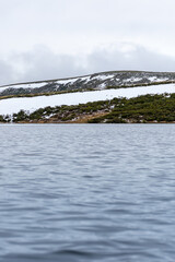 Vertical panoramic landscape image from a boat in the middle of the water with snowy mountains in the background on a cloudy day