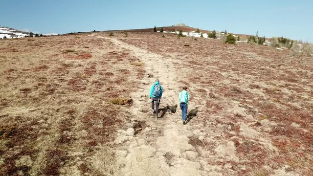 A drone capture of a couple with big backpacks hiking to Seiner Kreuz, a peak in Austrian Alps. Cross on the peak. There are a few snow fields around. Early spring in the mountains. Wanderlust
