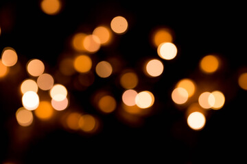 Obraz premium Bokeh lights background in yellow and lilac colors on black. Christmas lights string garland, festive overlay