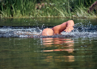 Man swims freestyle in open water on the river in summer