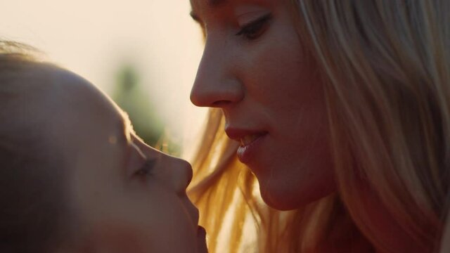 Woman kissing girl in city park. Daughter licking mother nose outdoor.