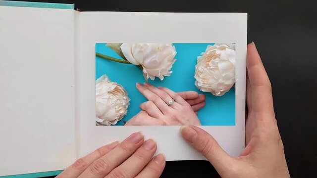 A woman's hand opens a photo album and a photography comes to life with a memory where a marriage proposal is made. Romantic concept.