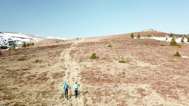 A drone capture of a couple with big backpacks hiking to Seiner Kreuz, a peak in Austrian Alps. Cross on the peak. There are a few snow fields around. Early spring in the mountains. Wanderlust
