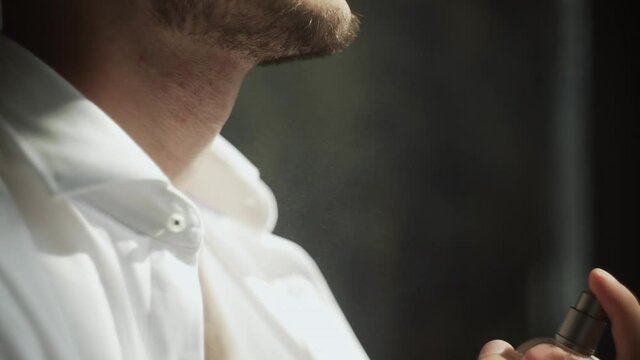 Bearded handsome businessman in a white shirt sprinkles perfume on himself