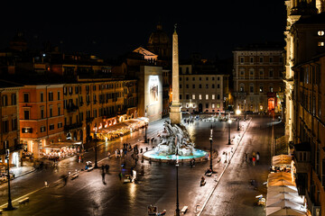 View from a window overlooking Piazza Navona at night showing the illuminated cathedrals, sidewalk cafes, tourists and the fountain of the Four Rivers