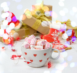 large ceramic cup with cocoa and marshmallows, behind a gift box and a Christmas garland