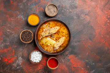 top view bowl of chicken soup around different spices on dark red background with copy space