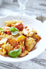 Pasta with chicken breast, cherry tomatoes and fresh basil. Bright wooden background. Close up. 