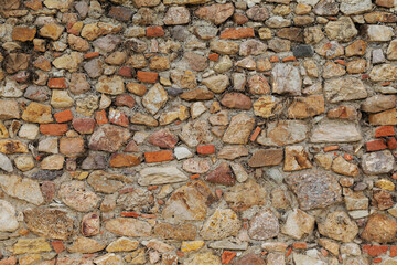 Colorful brick wall with structure of white, grey and brown stones, uneven and empty facade as a background with space for text