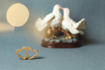Two wooden hearts joined together on a gray background. Statuette with kissing pigeons in the background, blurred background, bokeh effect