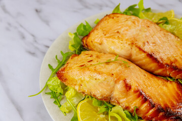 Fried salmon fillet with green salad on white plate.