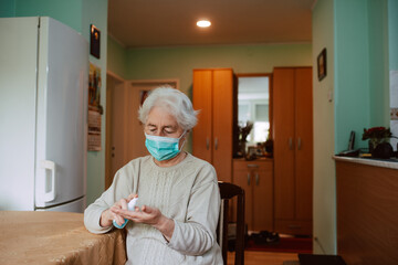 A cute senior grandmother who pours an antibacterial hand sanitizer into her hand while sitting at a table in the house. Hand hygiene during isolation of COVID-19 coronavirus
