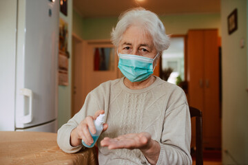Portrait of a senior woman with a mask pouring an antibacterial hand sanitizer into her hand while sitting at a table. Hygiene during the COVID-19 coronavirus pandemic