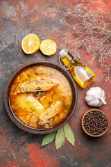 top view chicken soup a bowl of black pepper bay leaves lemon slices oil garlic on dark red background