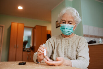 Portrait of a senior woman with a mask holding a blood sugar meter and testing blood from a finger...