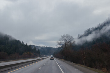 Highway with road signs on the sides among high mountains in the clouds in winter, along which trucks and cars travel. Idaho, USA, 12-5-2020