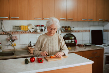 Senior caucasian woman cooking lunch and chopping vegetables on a board in the kitchen. A retired lady while cooking lunch for her family in the kitchen