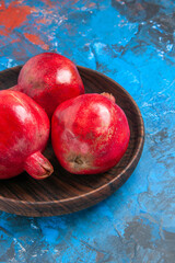 Half shot of a brown plate with full fresh pomegranates on the left side on isolated blue background in vertical view