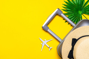 Summer time. Travel accessories with suitcase, white plane, palm leaves in minimal trip vacation concept on yellow background. Exotic tropical beach with copy space.