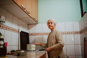 Caucasian grandmother cooking lunch in the kitchen. A gray-haired retired woman next to a kitchen stove