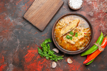 top view chicken and rice soup in a bowl hot peppers bowl with sea salt garlic parsley leaves a chopping board on dark red background with copy space