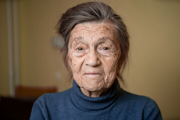 Elderly Caucasian senior grandmother ninety years old looks attentively and smiles, feels happy, large portrait, face with deep wrinkles, gray hair. Theme pensioners, old people and long-lived woman