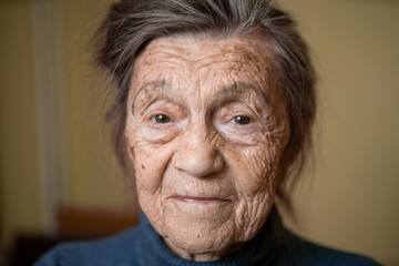 90 year old cute elderly woman with gray hair and wrinkles face, wearing sweater, portrait large, smiling and looking joyfully, background of room. Theme long-liver and aging, old people in good mood