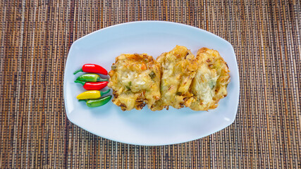 Traditional Indonesian Snack Bakwan ,vegetable fritter made from corn, carrot and cabbage served with red chili on wricker background