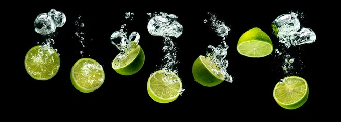 Fototapeten Bunch of lime fruits halves sinking with bubbles into water isolated against black background. Citrus theme, panorama © Przemyslaw Iciak