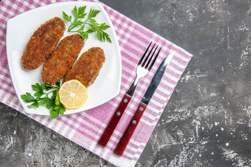 top view cutlets lemon slice parsley on white plate fork and knife kitchen towel on grey background with copy space