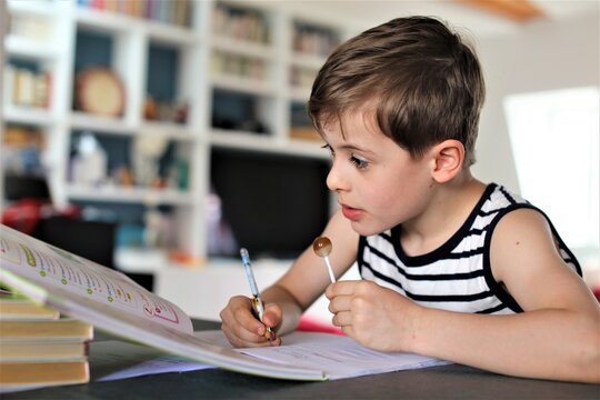 Enfant qui se concentre en faisant ses devoirs et en mangeant une sucette