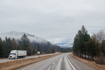 Highway with road signs on the sides among high mountains in the clouds in winter, along which trucks and cars travel. Idaho, USA, 12-5-2020