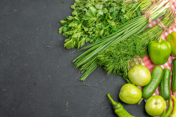 Collection of greens and fresh various organic vegetables on orange stripped towel on dark background